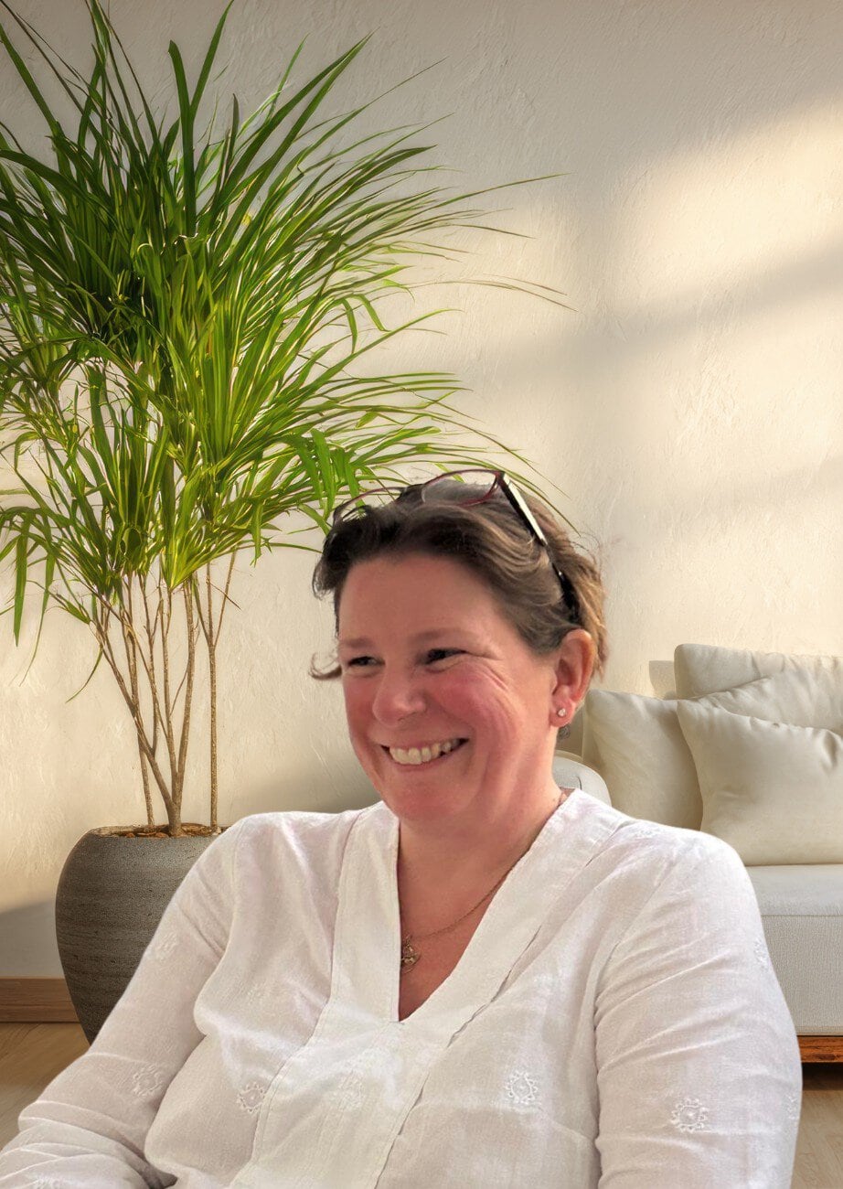 Professional woman smiling in a bright, welcoming office setting with a large green plant.